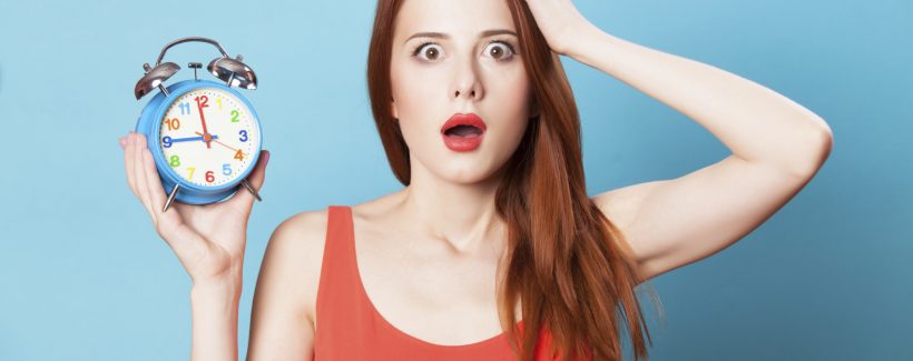 Surprised redhead women woth alarm clock on blue background.